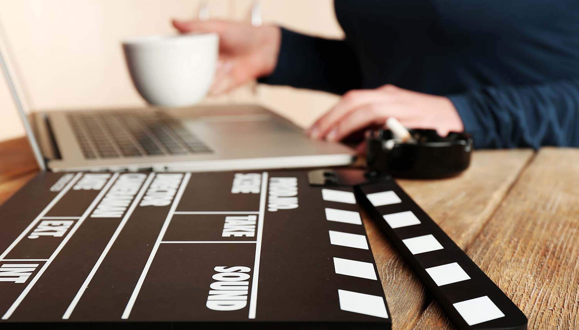 A person drinking coffee while typing on their laptop next to a film set clapper