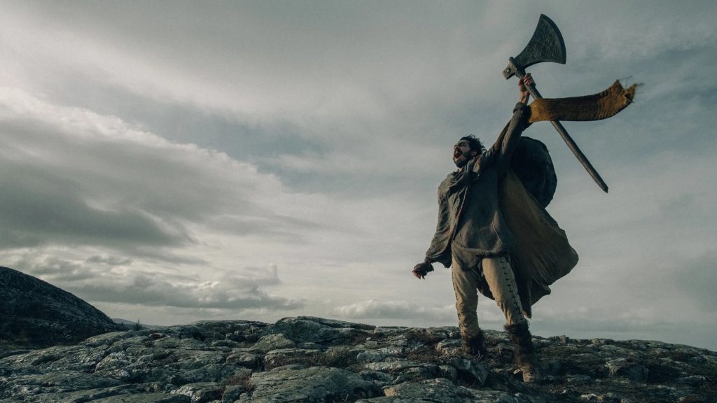 Sir Gawain (Dev Patel) holding up an ax in celebration in 'The Green Knight,' Journey Beyond Reality: Fantasy Films That Ignite the Imagination