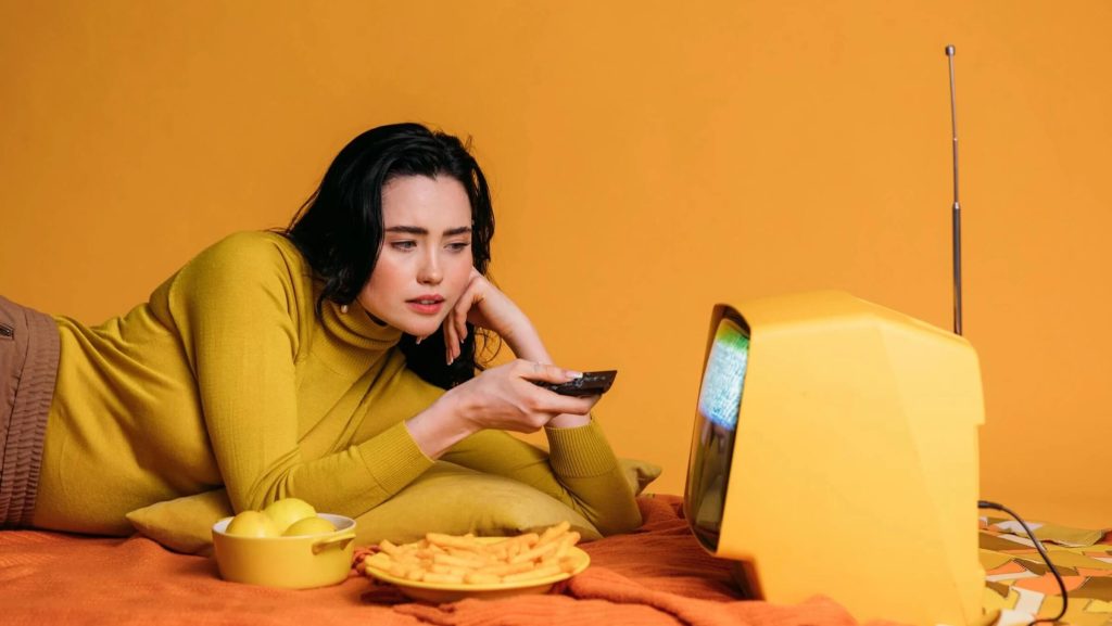 Woman in Yellow Long Sleeve Shirt Watching Tv In Bed