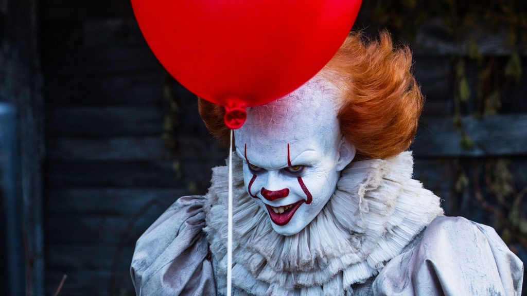 Pennywise (Bill Skarsgård) holding a red balloon in 'It,' Demons, Dark Lords, and Other Big Bads: The 13 Best Villains in Cinematic History
